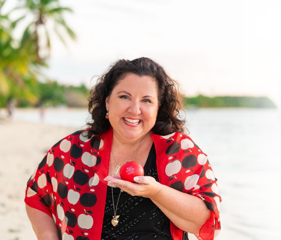 Dr. Lisa Hartwell on the beach in an apple-print wrap, holding a red Bad Apples stress ball